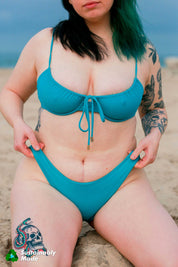 Rooted Swim Classic Bikini Bottom in the color Calypso, a medium coverage bottom. Displaying a photo of the front of the teal blue bottoms