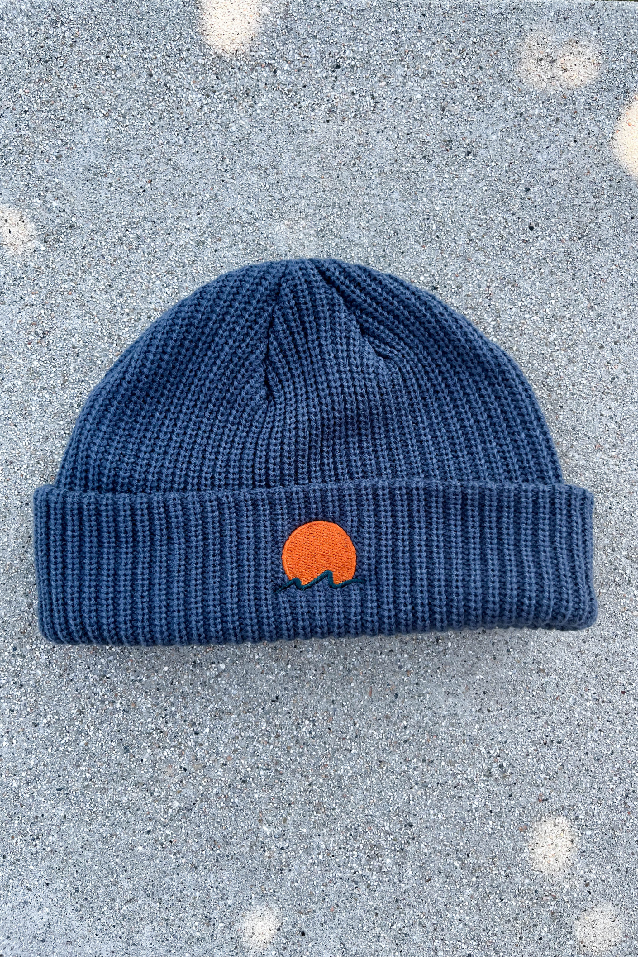 Classic cuffed knit fisherman beanie featuring embroidered Rooted Swim sunset logo in a blue gray color. high quality knit beanie