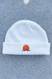 person wears a classic cuffed knit fisherman beanie featuring embroidered Rooted Swim sunset logo in a soft warm white color. high quality knit beanie