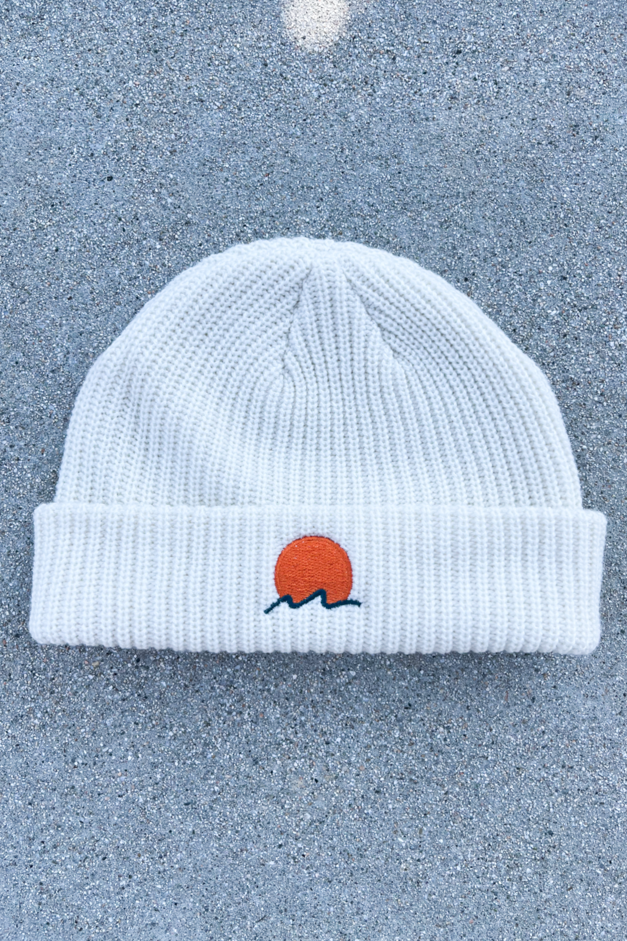 person wears a classic cuffed knit fisherman beanie featuring embroidered Rooted Swim sunset logo in a soft warm white color. high quality knit beanie