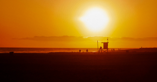  Image of Newport beach sunset with bright orange sky, sun and lifeguard tower