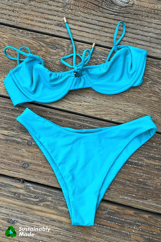 Rooted Swim Classic Bikini Bottom in the color Calypso, a medium coverage bottom. Displaying a photo of the teal blue bottoms with the matching front tie balconette top