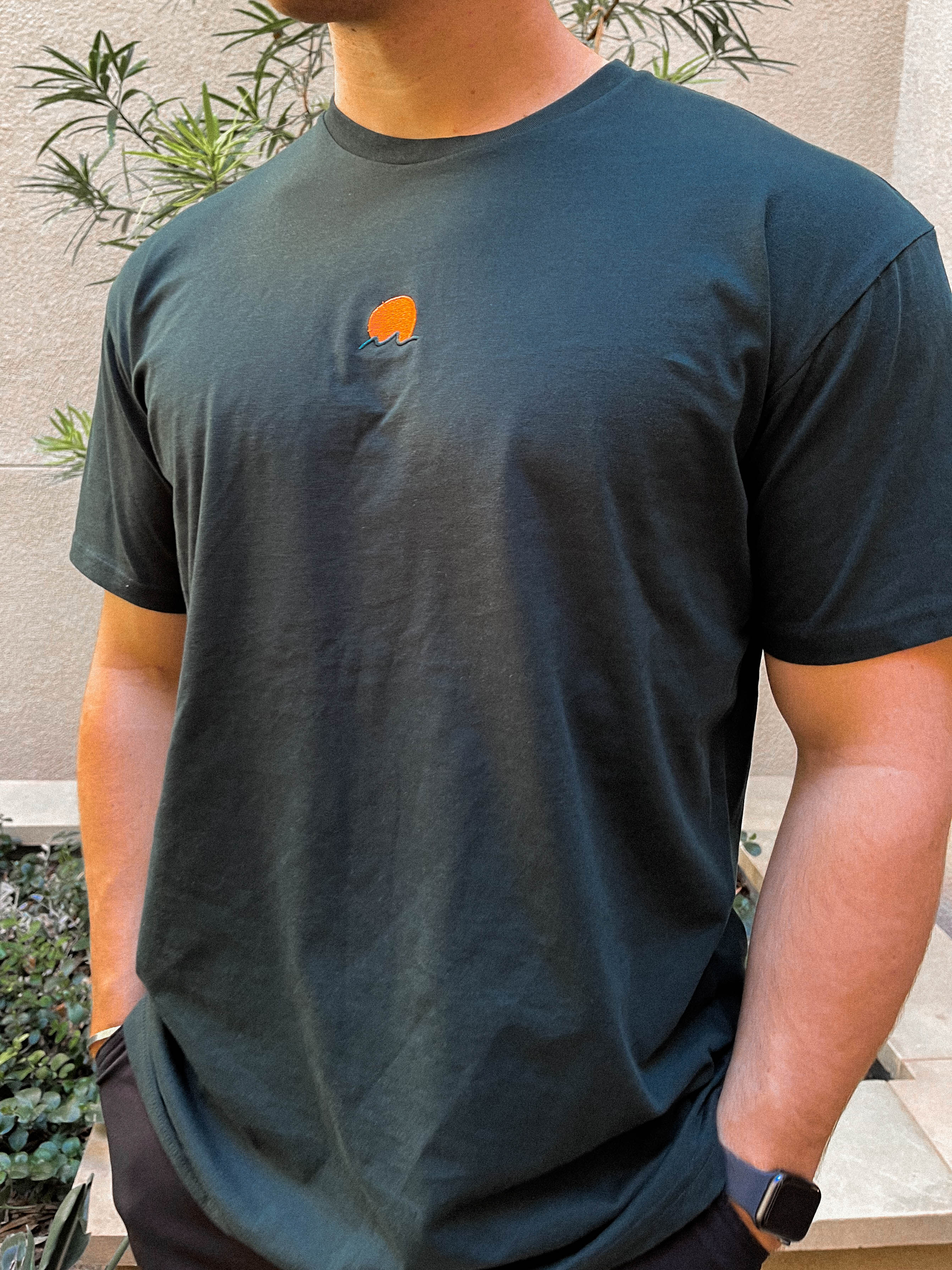 Rooted Swim Sunset Embroidered Tee Shirt in Pine Green. Includes red sun and dark green wave design.